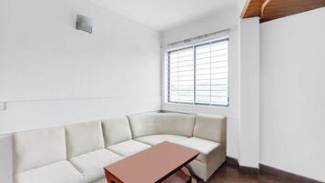 A corner room with a white textured sofa, a wooden table, and a window with blinds.
