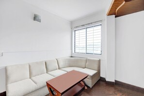 A corner room with a white textured sofa, a wooden table, and a window with blinds. - Townhouse Mysore City Centre (Mysore)