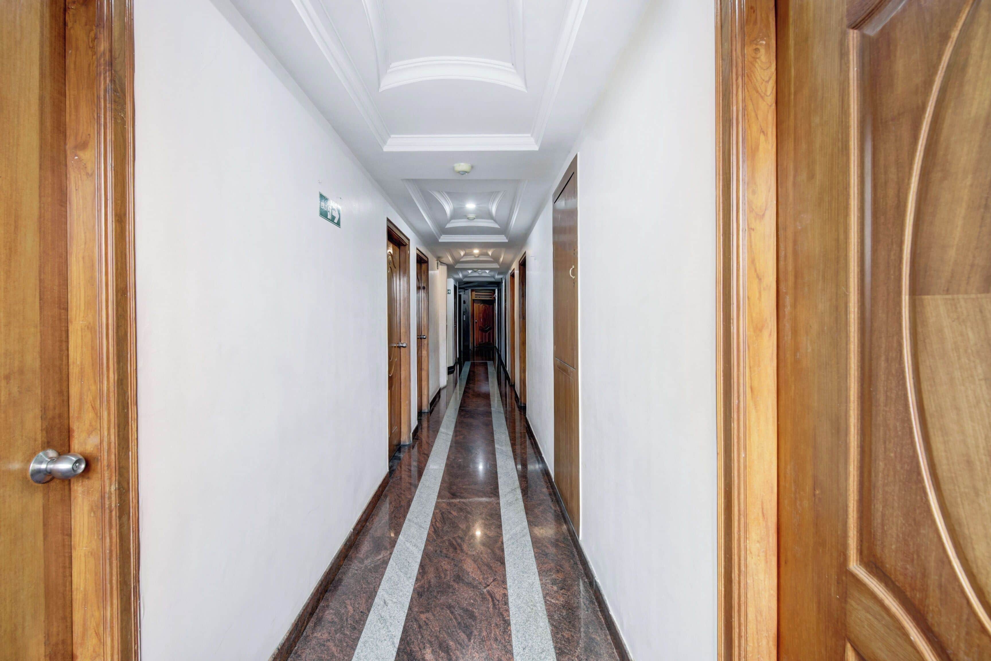 A hotel corridor with wooden doors, white walls, and a marble floor.