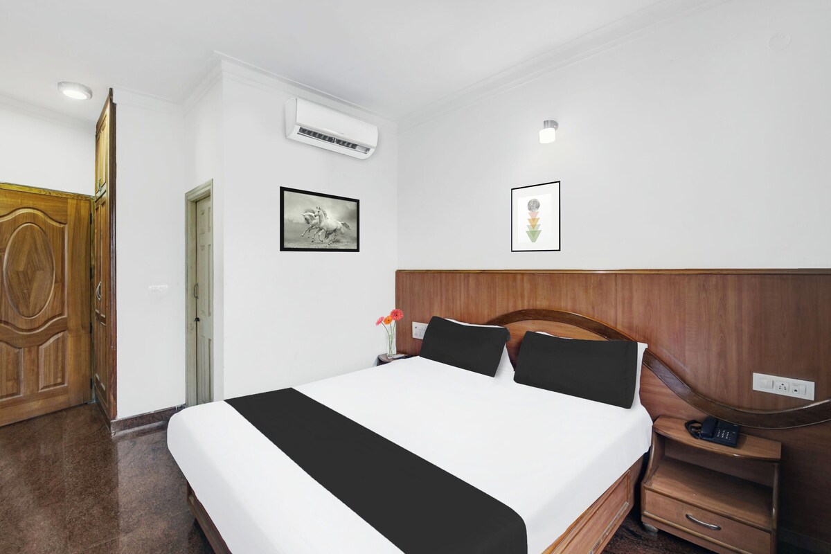 A hotel room with a bed, a nightstand, a wooden wardrobe, an air conditioning unit, a framed picture, and a wall-mounted light.
