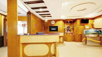 A hotel reception area with a wooden reception desk, a clock, and a TV mounted on the wall.