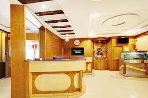 A hotel reception area with a wooden reception desk, a clock, and a TV mounted on the wall. - Townhouse Mysore City Centre (Mysore)