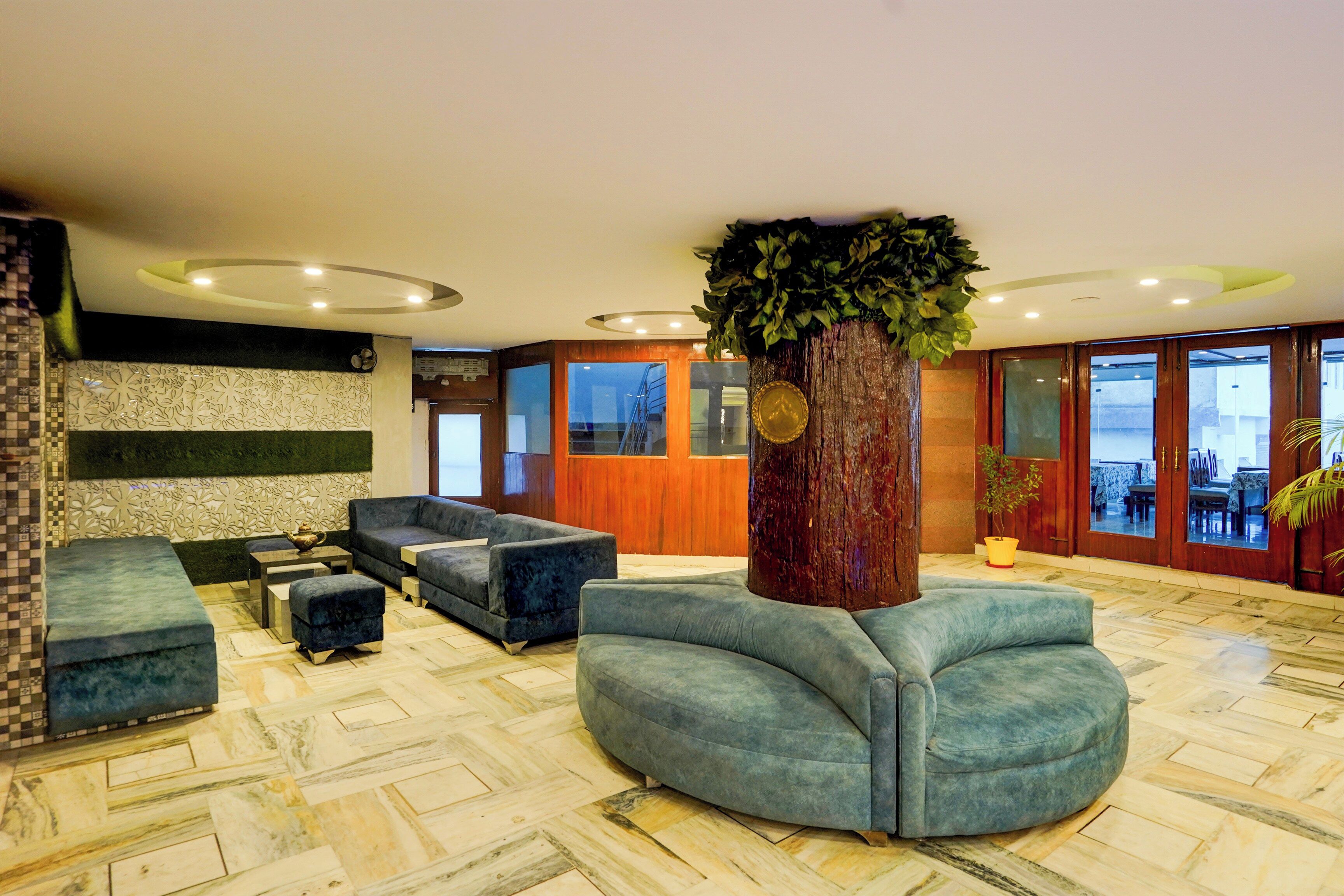 Vestíbulo de hotel con mostrador de recepción, zona de estar con sofás, una planta decorativa y un suelo con patrón de espiga.