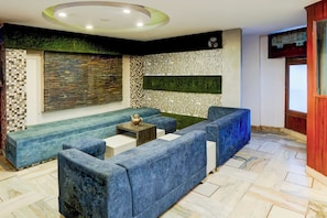 Un área de descanso moderna con sofás azules, una mesita con un objeto decorativo y una pared con paneles ornamentales y un detalle en verde.