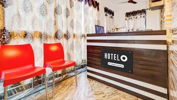 A hotel reception area with a wooden reception desk, two red chairs, and a marble floor.