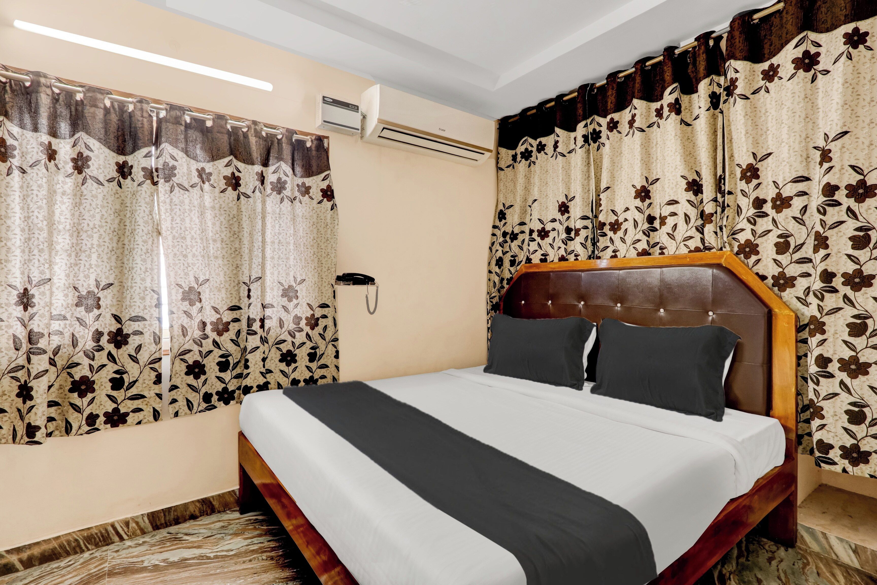 A hotel room with a bed, curtains, an air conditioning unit, and a telephone.