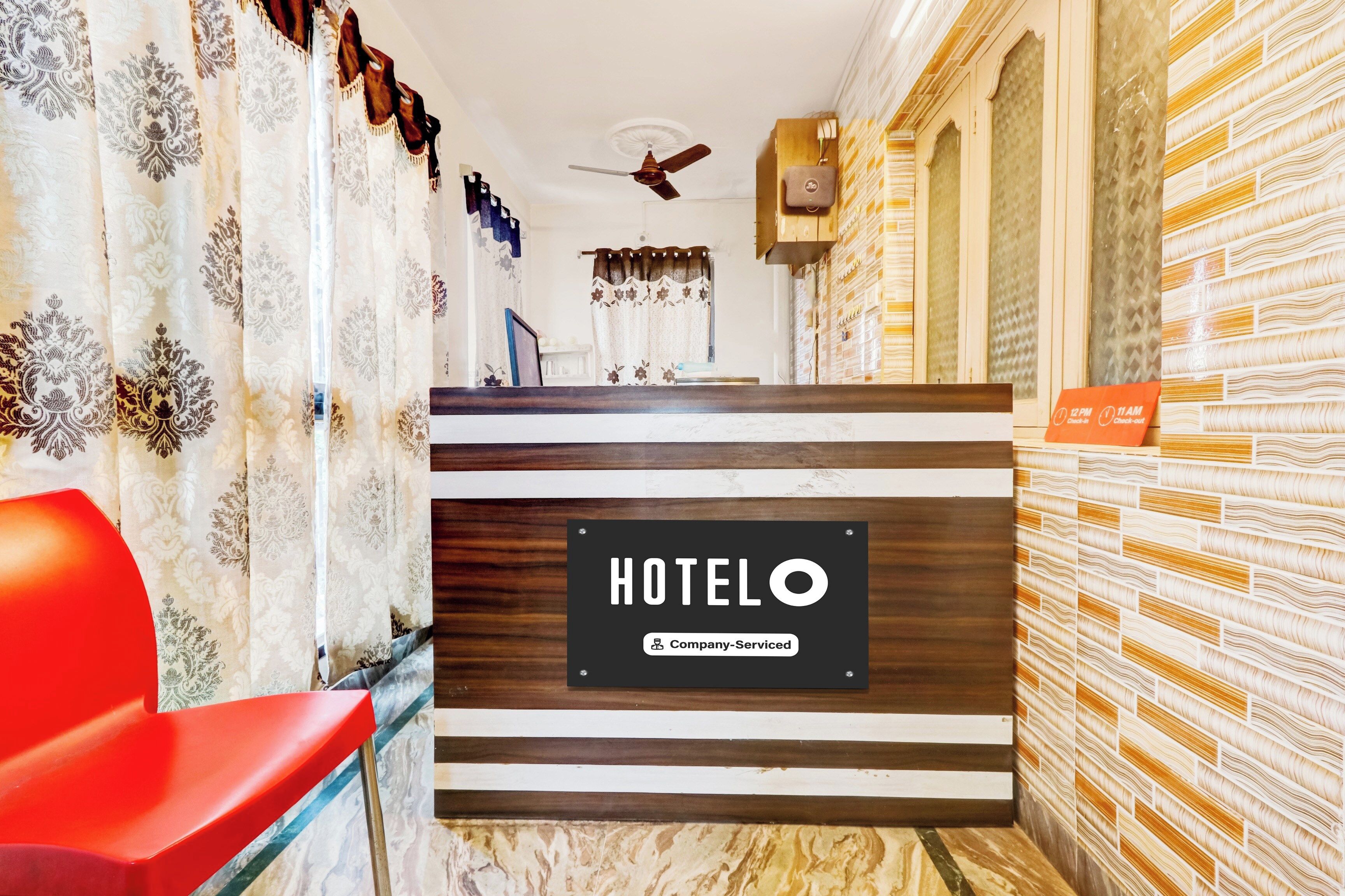 Un'area reception di un hotel dal design moderno, con una scrivania, una sedia rossa e una ventola a soffitto.