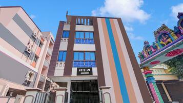 A hotel building with a sign indicating it is company-serviced. It features a modern design with a vertical striped facade and a gated entrance.