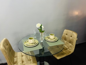 Ein runder Glastisch mit zwei Stühlen, jeder mit einer grünen Tischdecke und einer weißen Tasse und Untertasse. Auf dem Tisch steht ein weißes Blumenarrangement in einer klaren Vase.