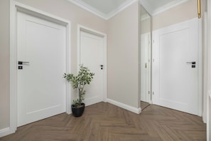 A hallway with white doors, wooden flooring, and a potted plant.