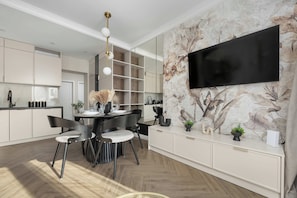 A modern kitchen with a dining area, a flat-screen TV mounted on the wall, and a chandelier. - Kielce | Żelazna 43 | Modern Apartment | Whirlpool Bath (Kielce)