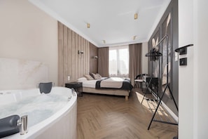 A modern bedroom with a large bed, a sitting area with a table and chairs, a bathtub, and a large window with curtains. - Kielce | Żelazna 43 | Modern Apartment | Whirlpool Bath (Kielce)