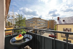 A balcony with a table and a bowl of fruit, overlooking a street with buildings and parked cars. - Kielce | Żelazna 43 | Modern Apartment | Whirlpool Bath (Kielce)
