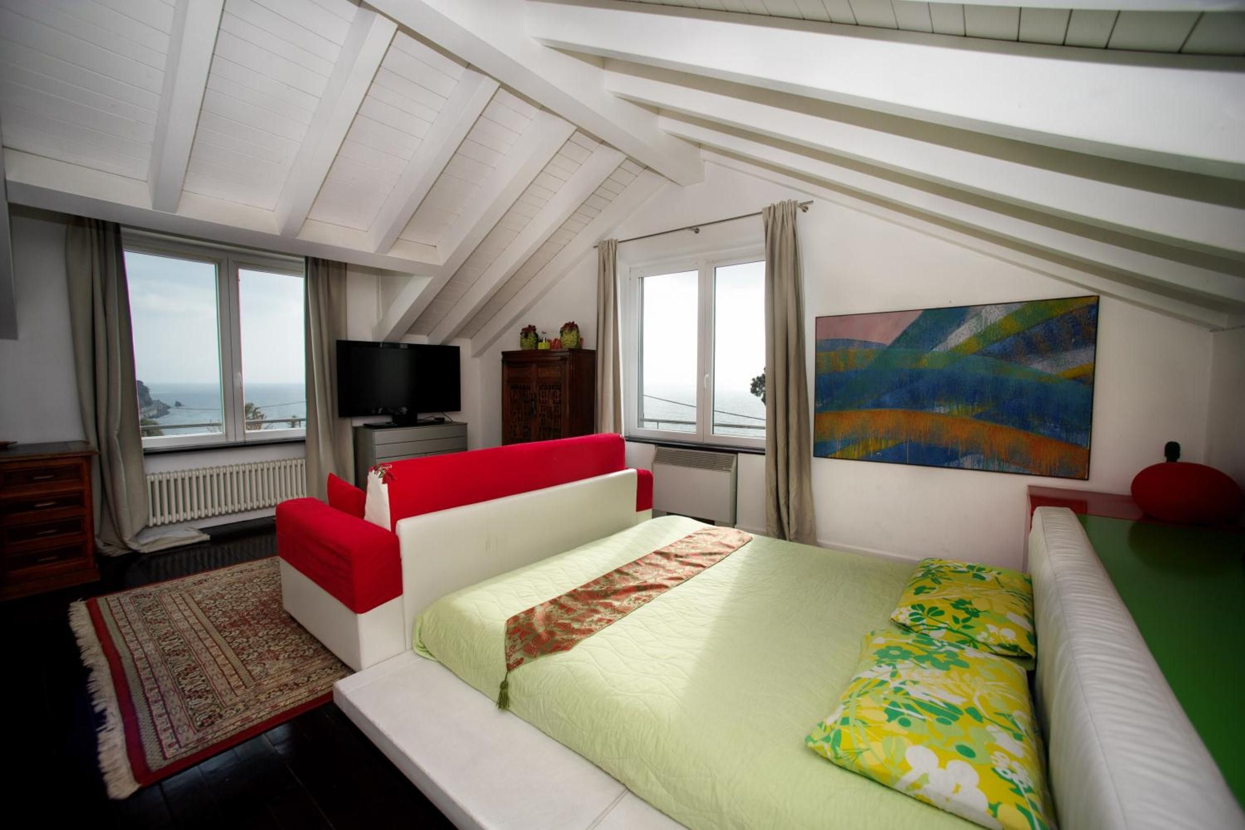 Une chambre à coucher avec un lit, une télévision, un tableau et une vue sur la mer.