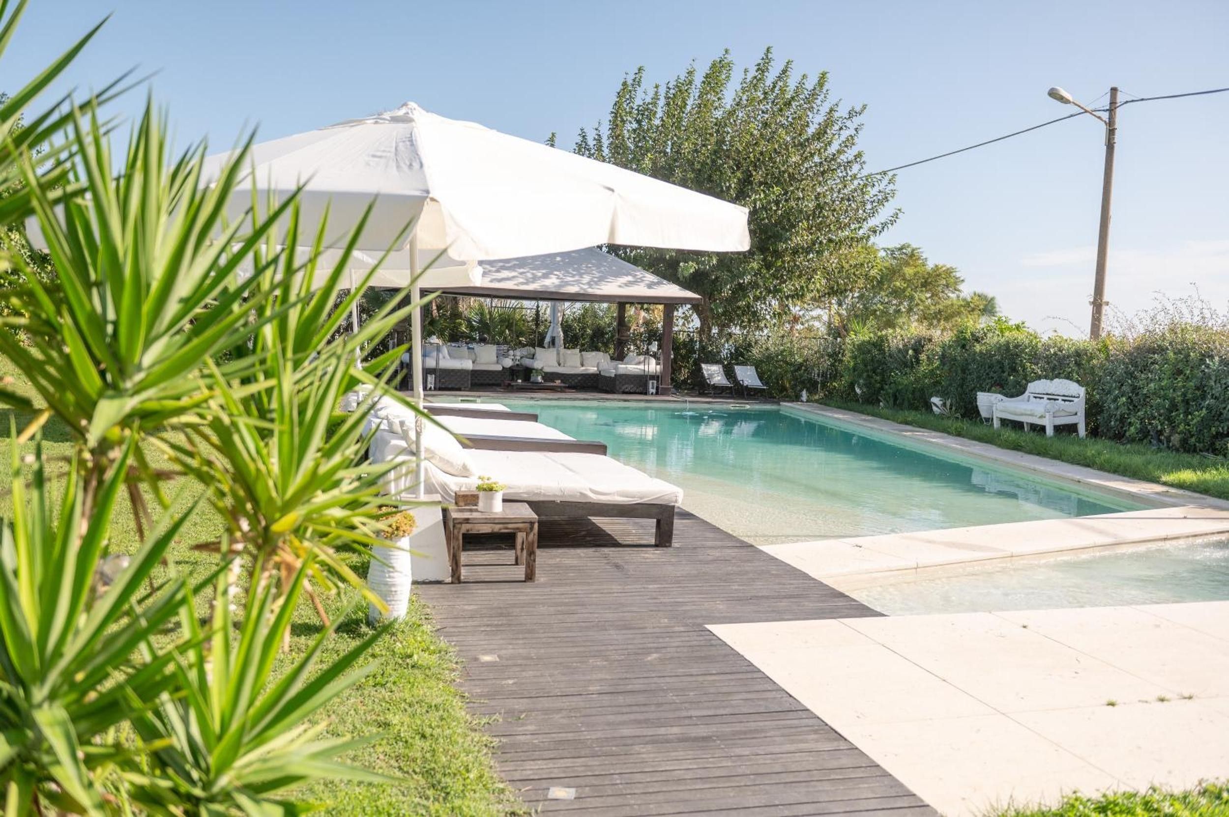 Un espace piscine doté d’une terrasse en bois, de chaises longues et d’un coin salon abrité.