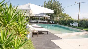 Un espace piscine doté d’une terrasse en bois, de chaises longues et d’un coin salon abrité.