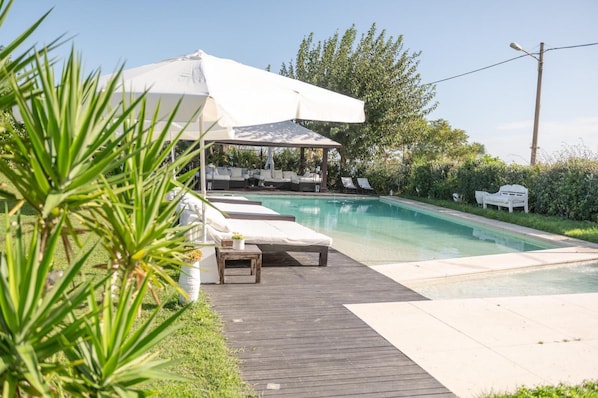 Ein Poolbereich mit Holzterrasse, Liegestühlen und einer überdachten Sitzgelegenheit.