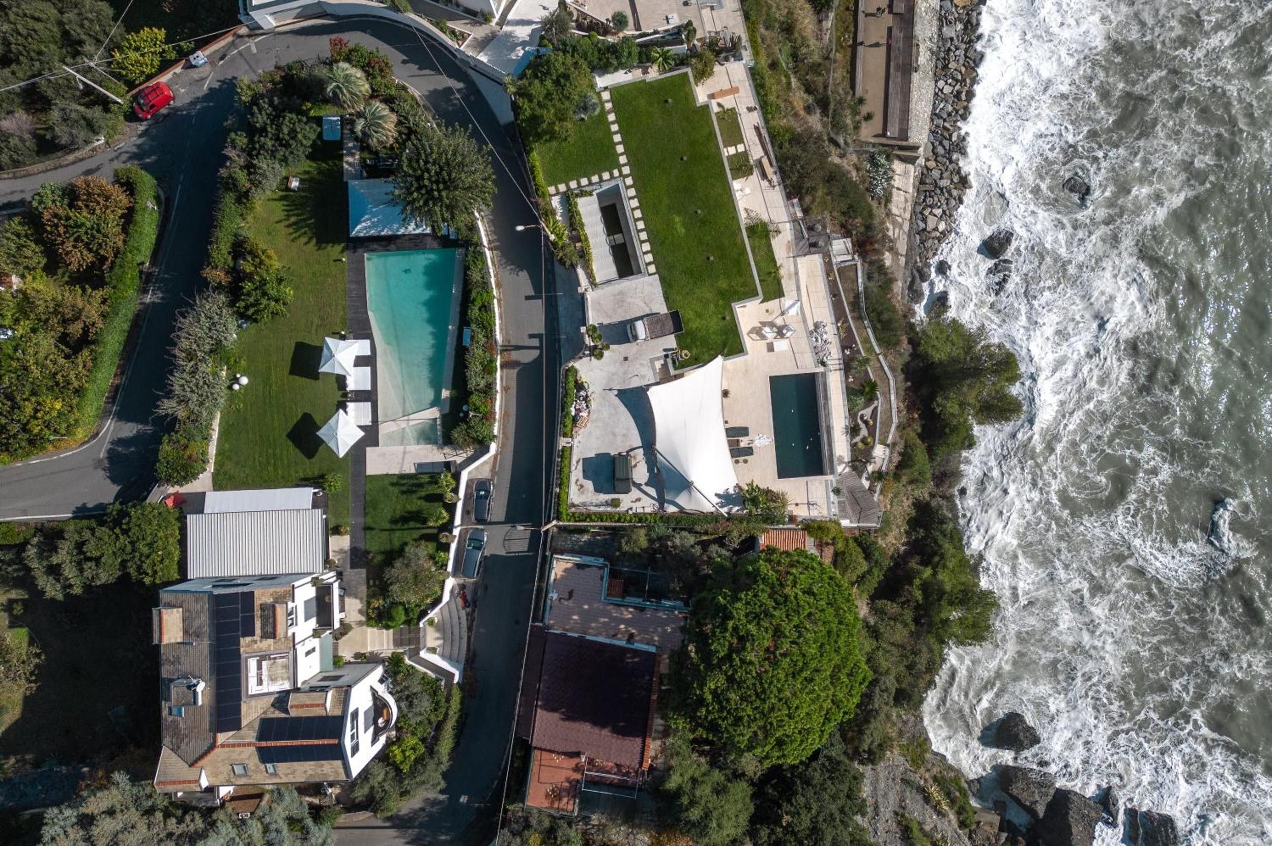 An aerial view of a coastal property with a swimming pool, a large house, and a view of the ocean.