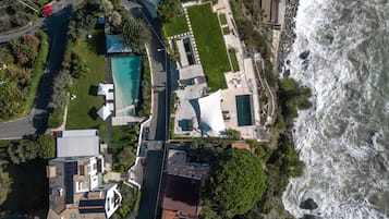 An aerial view of a coastal property with a swimming pool, a large house, and a view of the ocean.
