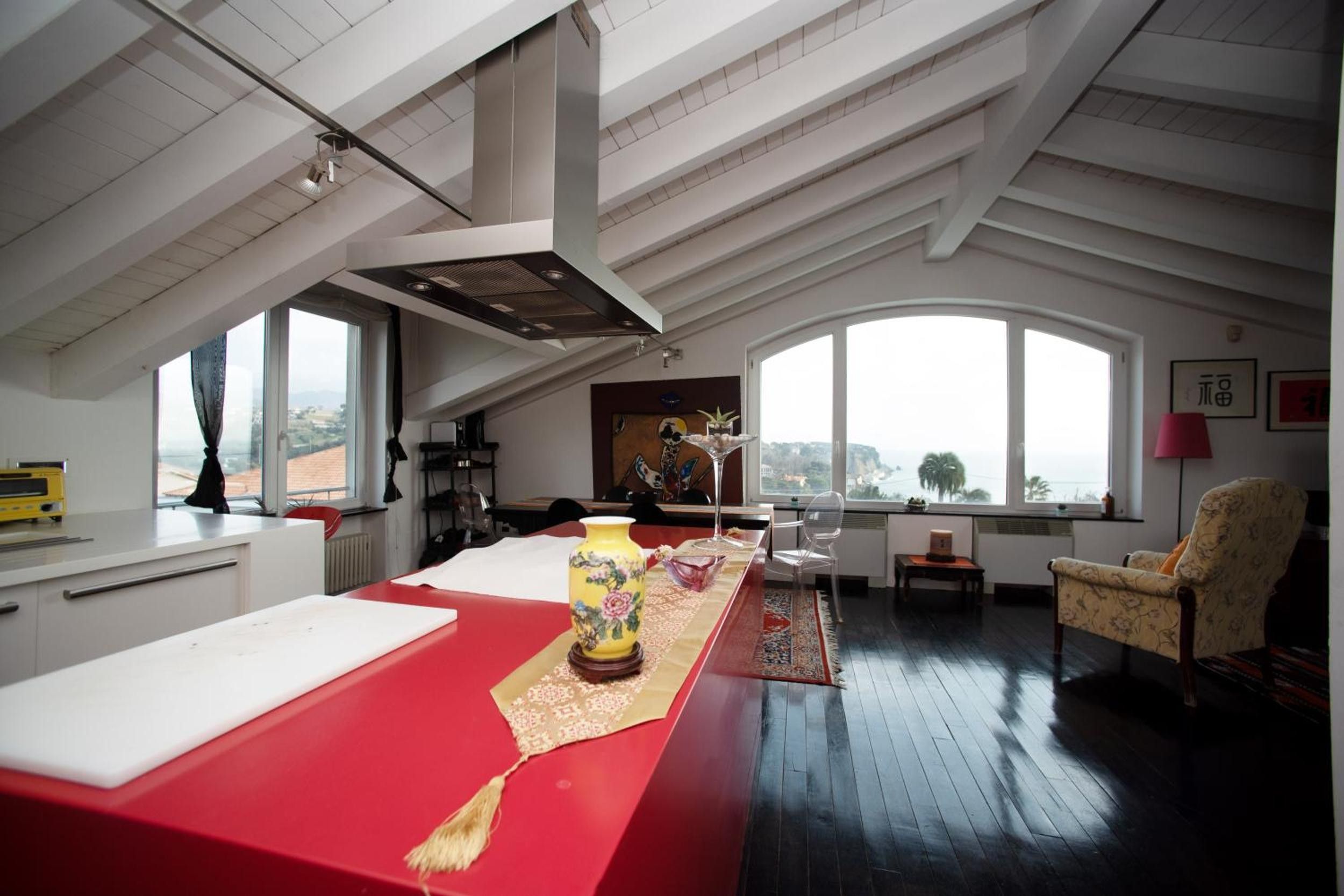 Quarto espaçoso com uma mesa vermelha, um vaso amarelo e uma janela grande com vista.