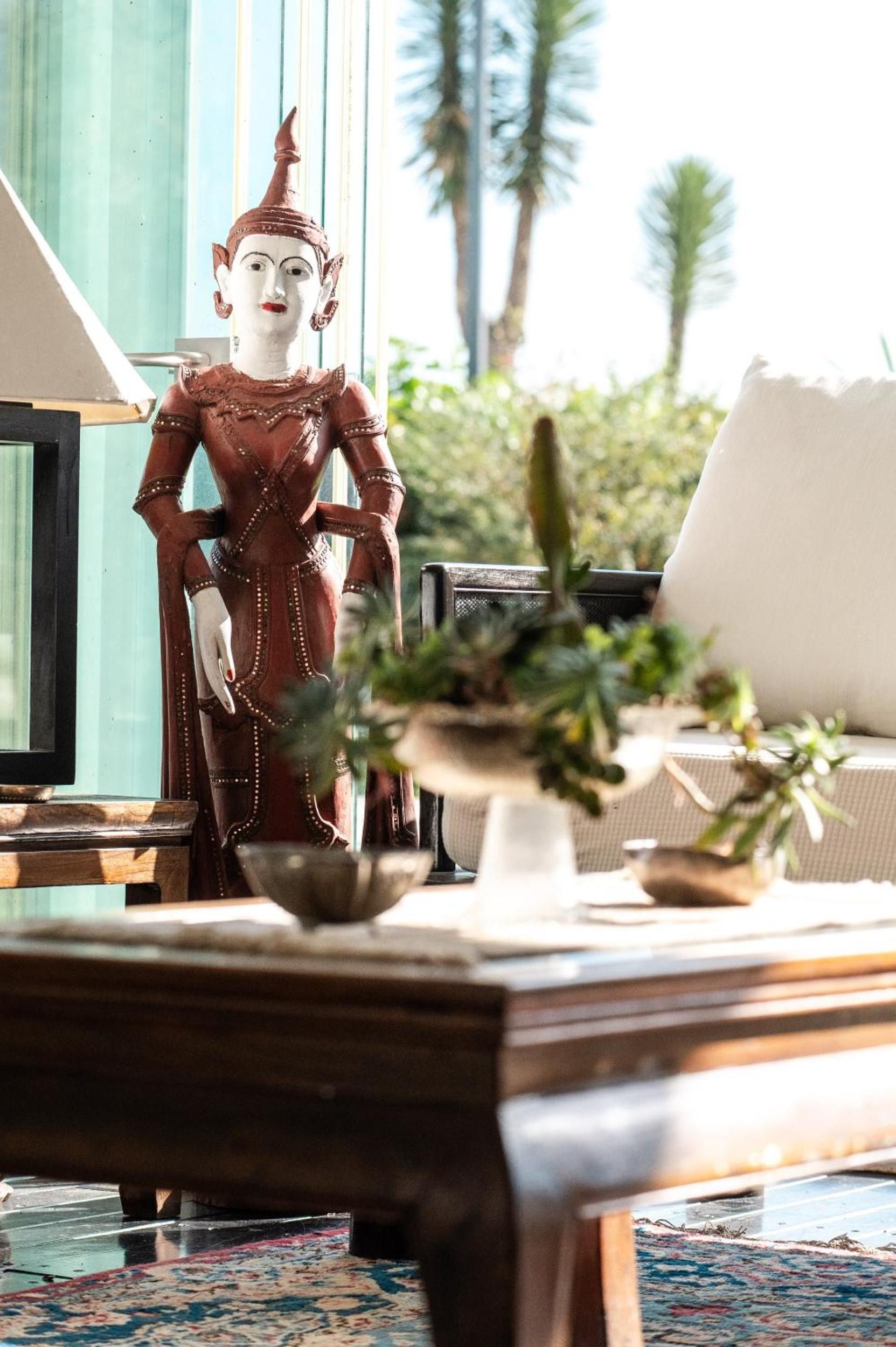 A statue of a figure in traditional attire, a potted plant, and a table with a vase and a bowl.
