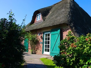 Ein traditionelles reetgedecktes Cottage mit Backsteinfassade, grünen Fensterläden und einem Weg zum Eingang.