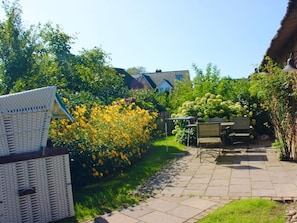 Ein Garten mit einer Terrasse, einem Korbstuhl und einer Bank.