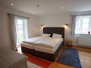Ein Schlafzimmer mit einem Doppelbett, zwei Nachttischlampen, einem kleinen Nachttisch, einem rot-weißen Teppich und einem Fenster mit Vorhängen.
