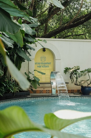 A pool with a waterfall feature, surrounded by lush greenery and a sign reading 'staymaster verdian'. - Staymaster Veridian (Goa)