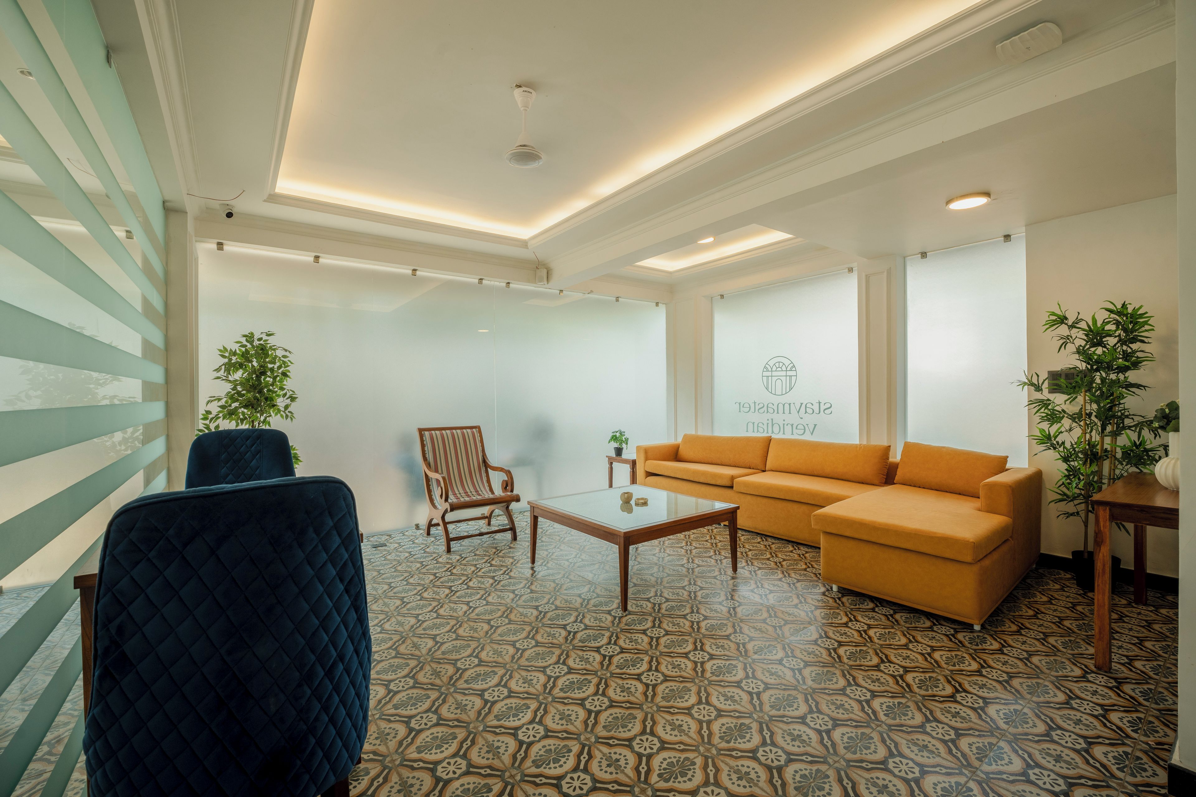 Una sala de estar moderna con piso estampado, un sillón azul, una mesa de centro de madera, un sillón a rayas y un sofá color mostaza.