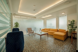 A modern living room with a patterned floor, a blue armchair, a wooden coffee table, a striped armchair, and a mustard-colored sofa. - Staymaster Veridian (Goa)