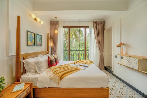 Habitación de hotel con cama, mesita de noche, ventana con cortinas y vista al exterior a zonas verdes.
