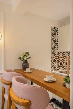 Un comedor con una mesa de madera, dos sillas rosas, un florero con flores y una pared con estampado.