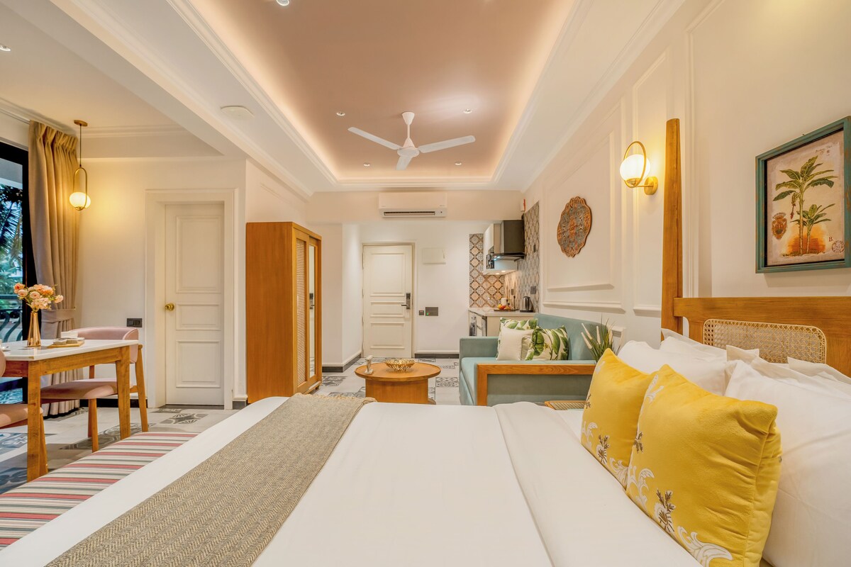 A hotel room with a bed, a desk, a chair, a sofa, a ceiling fan, and a wall-mounted TV.