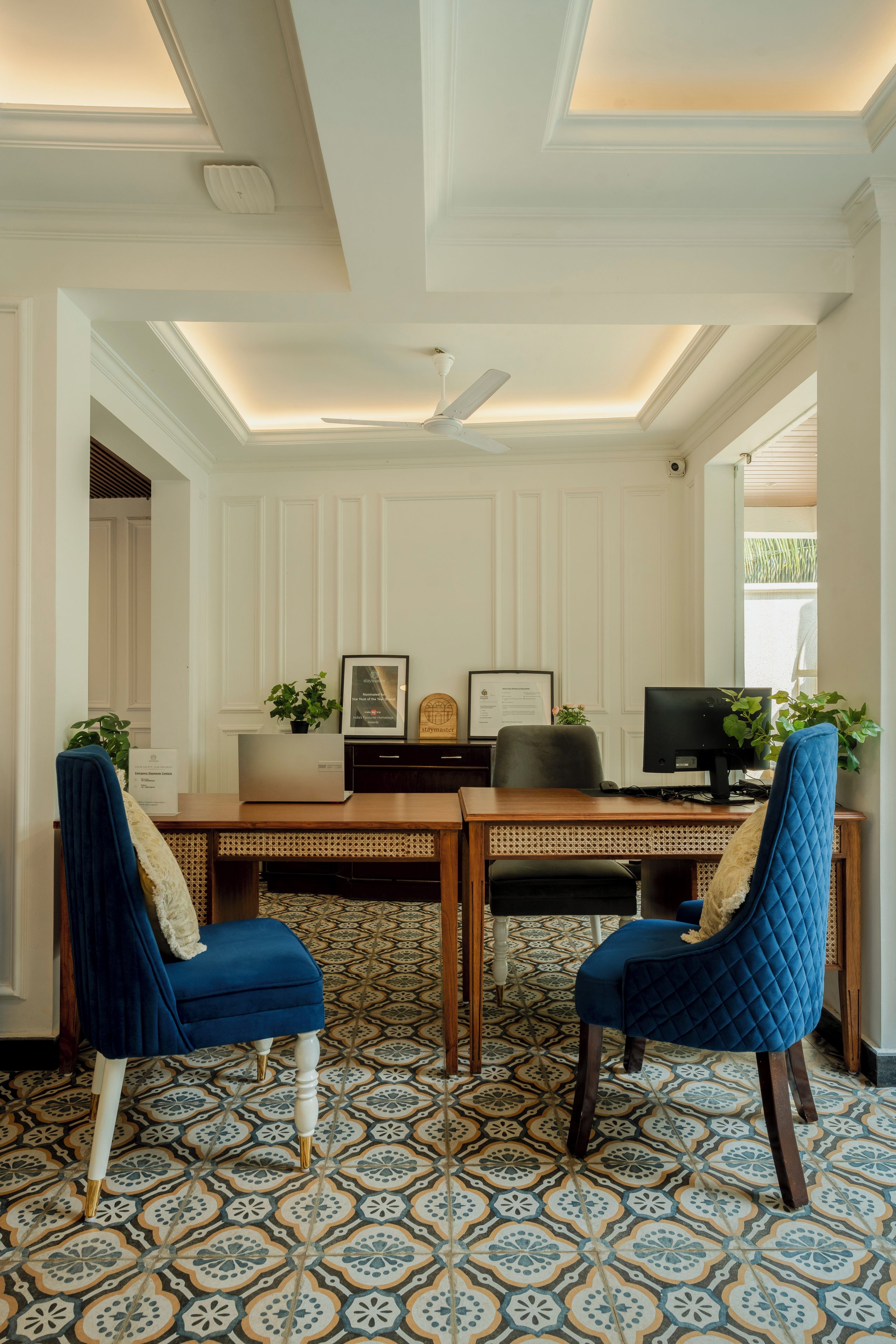Una habitación con escritorio, dos sillas, ventilador de techo y baldosas de suelo con diseño.