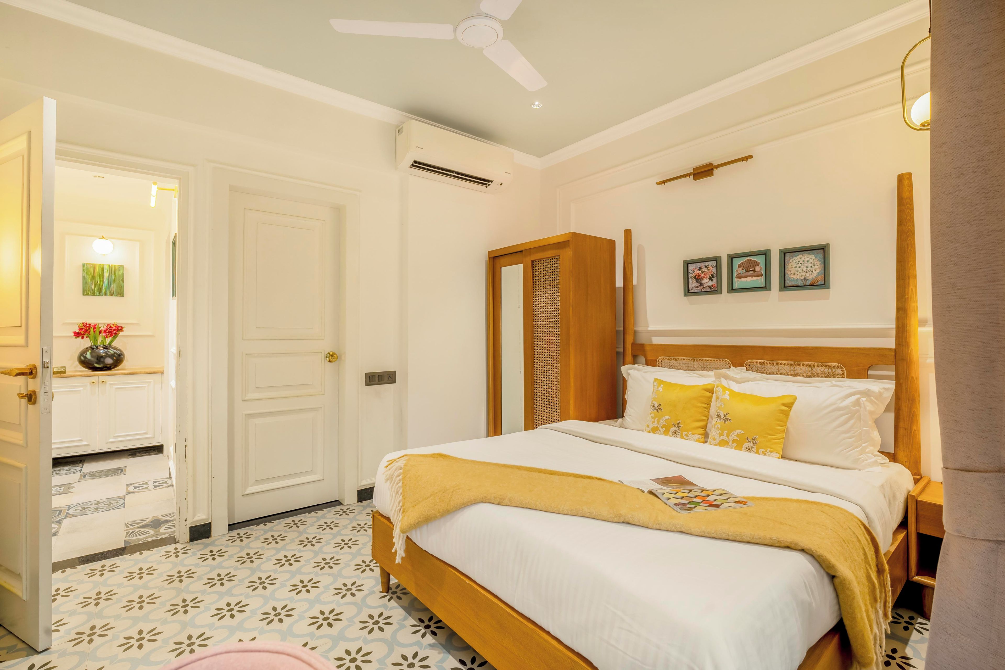 Une chambre d’hôtel avec un lit, une porte, un ventilateur de plafond et un mur orné de trois tableaux.