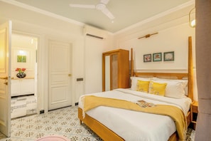 Habitación de hotel con una cama, una puerta, un ventilador de techo y una pared con tres cuadros enmarcados.