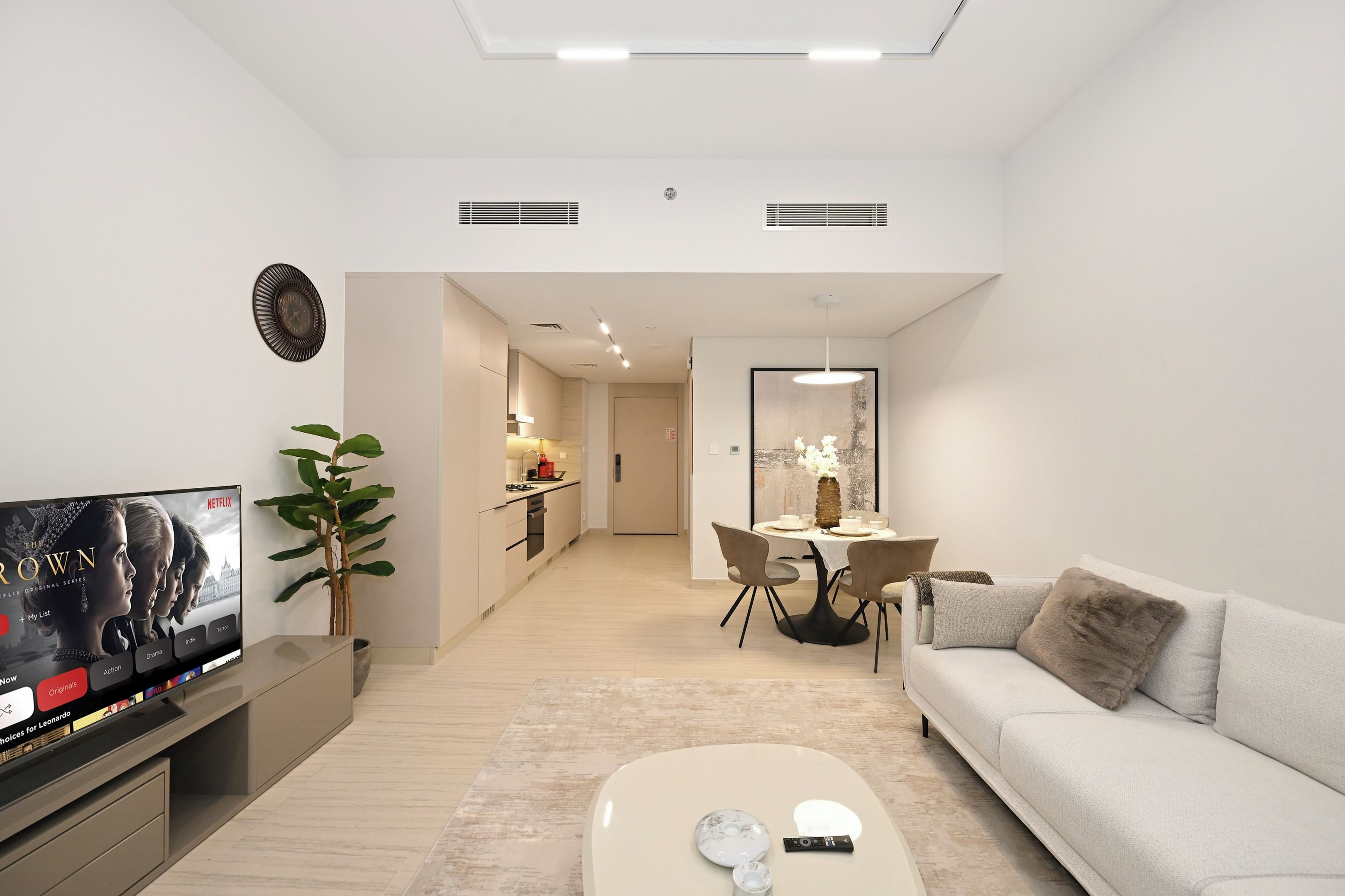 A modern living room with a flat-screen TV, a sofa, a coffee table, and a dining area with a table and chairs.