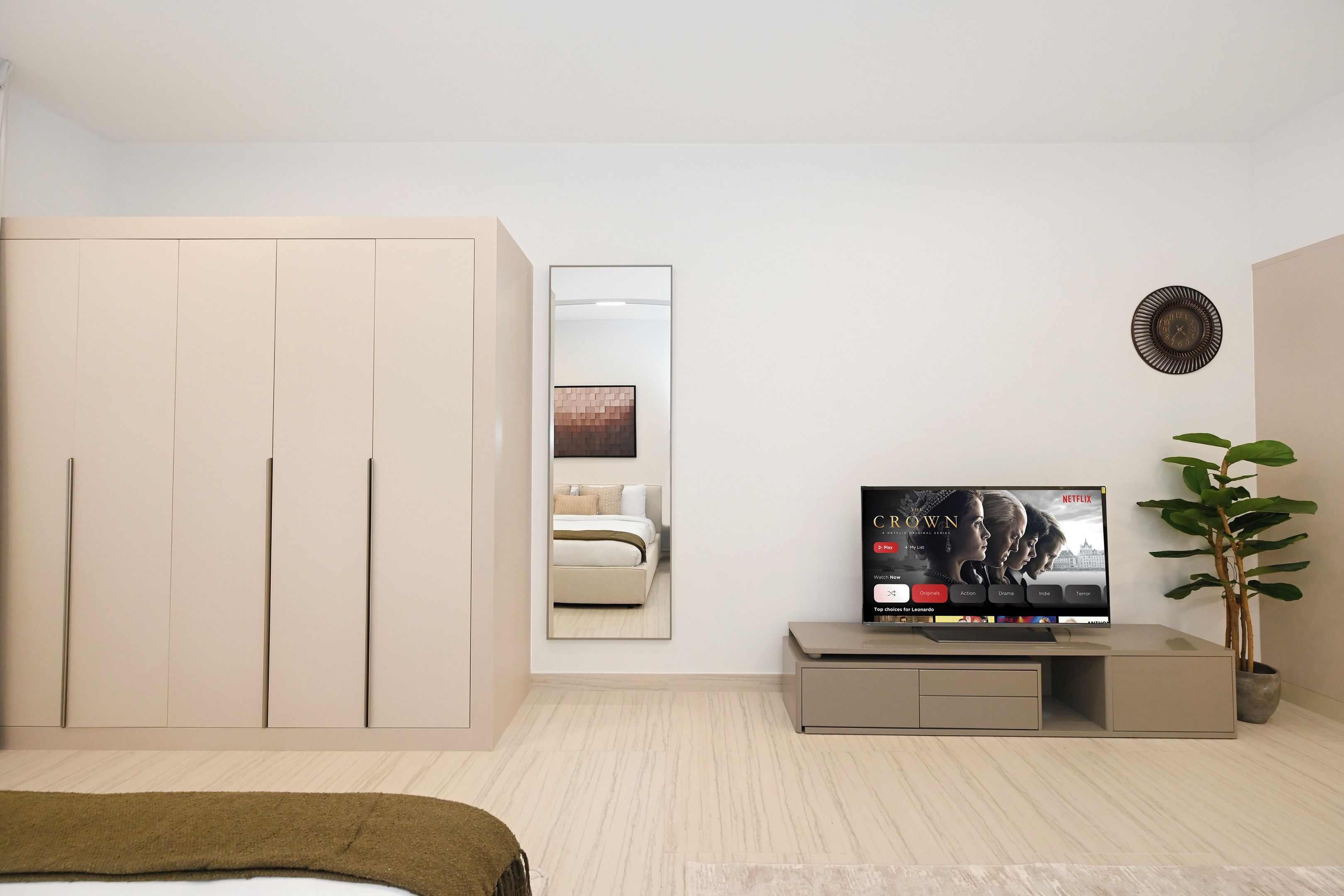 A modern bedroom with a bed, wardrobe, TV, and a plant.
