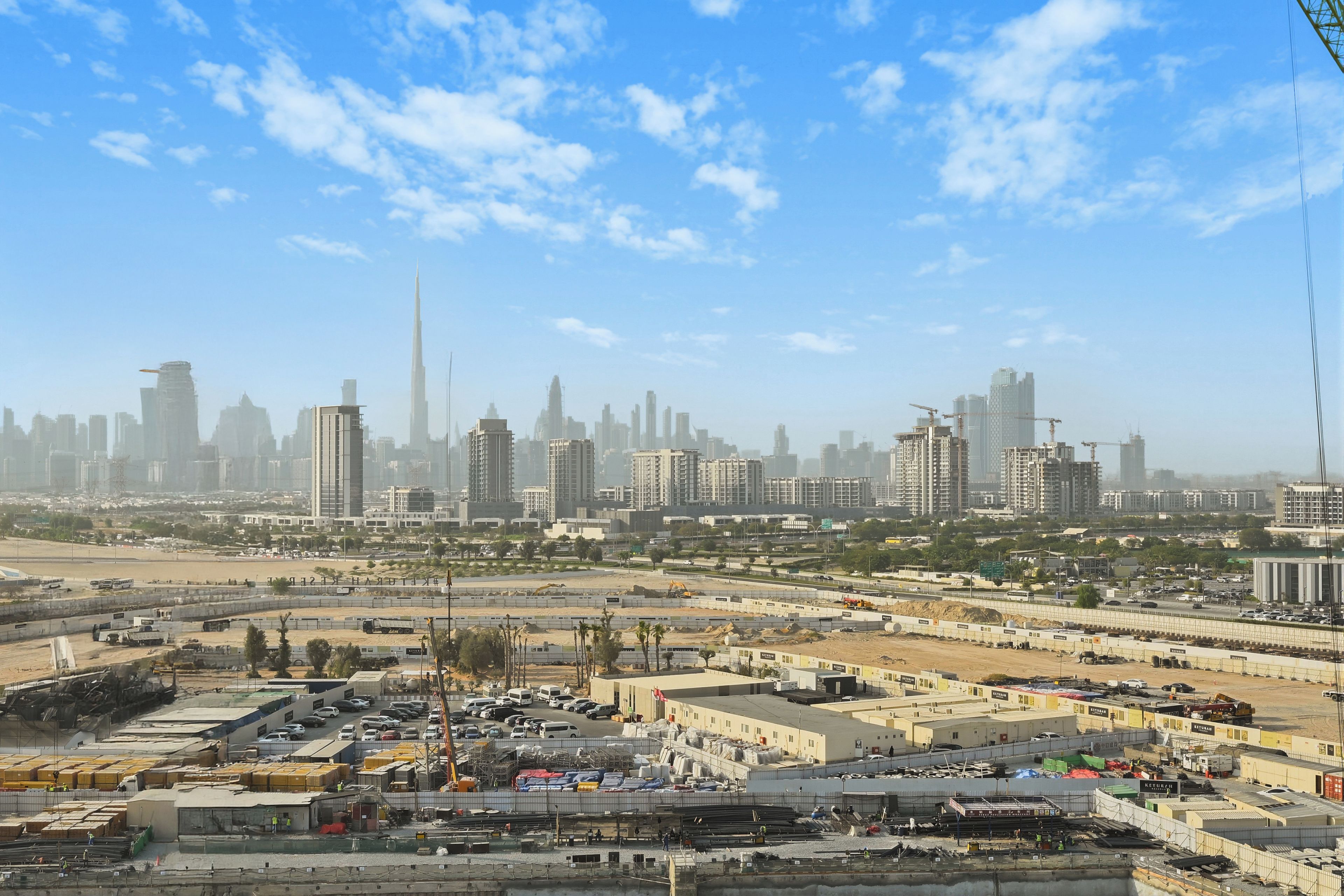 Une vue urbaine avec un gratte-ciel imposant, des chantiers de construction et un ciel dégagé.