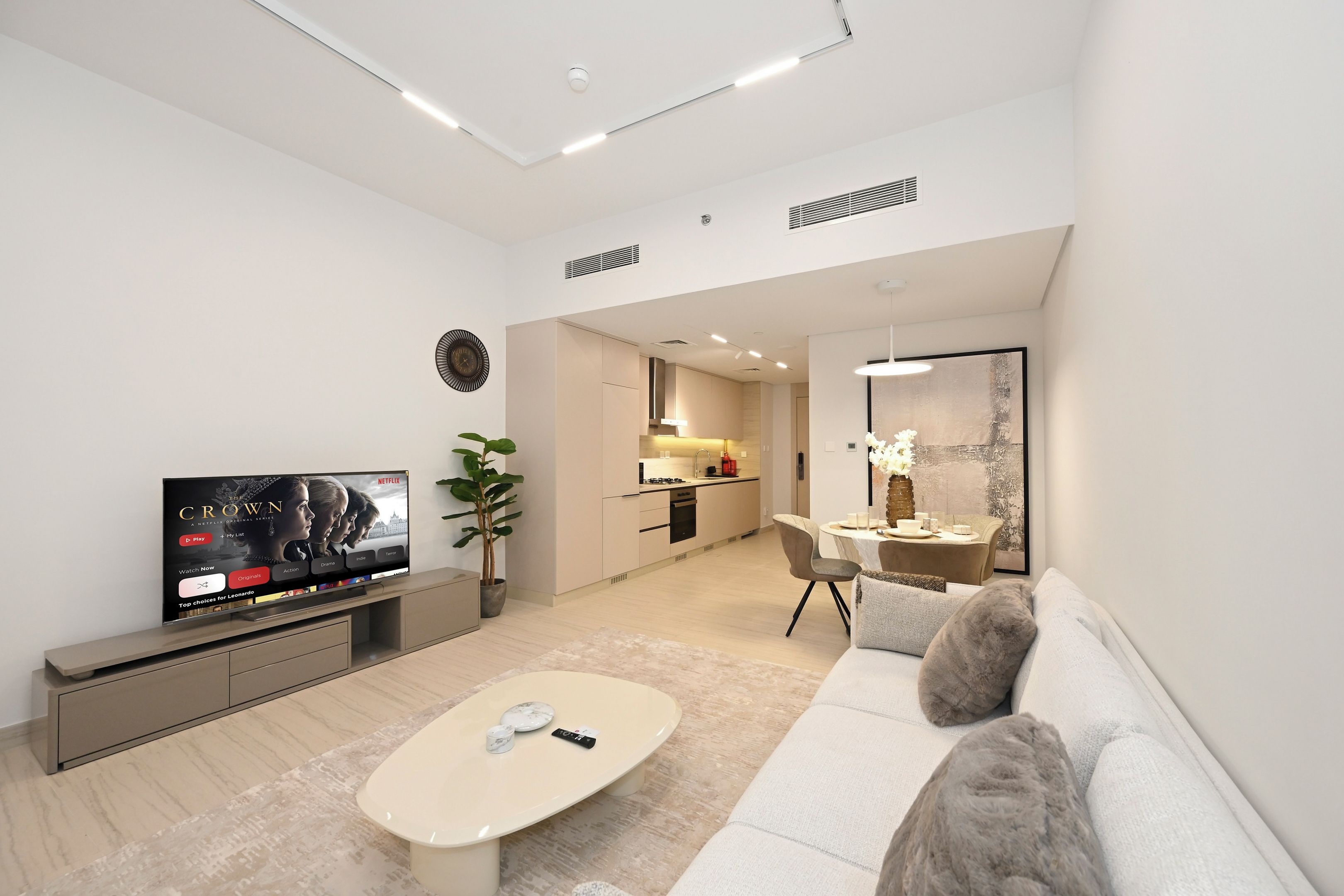 A modern living room with a flat-screen TV, a sofa, a coffee table, and a dining area with a table and chairs.