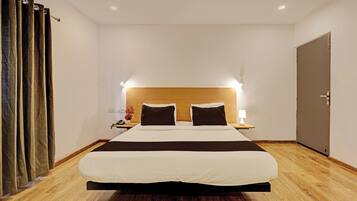A hotel room with a large bed, a wooden headboard, a bedside table with a lamp, and a door.