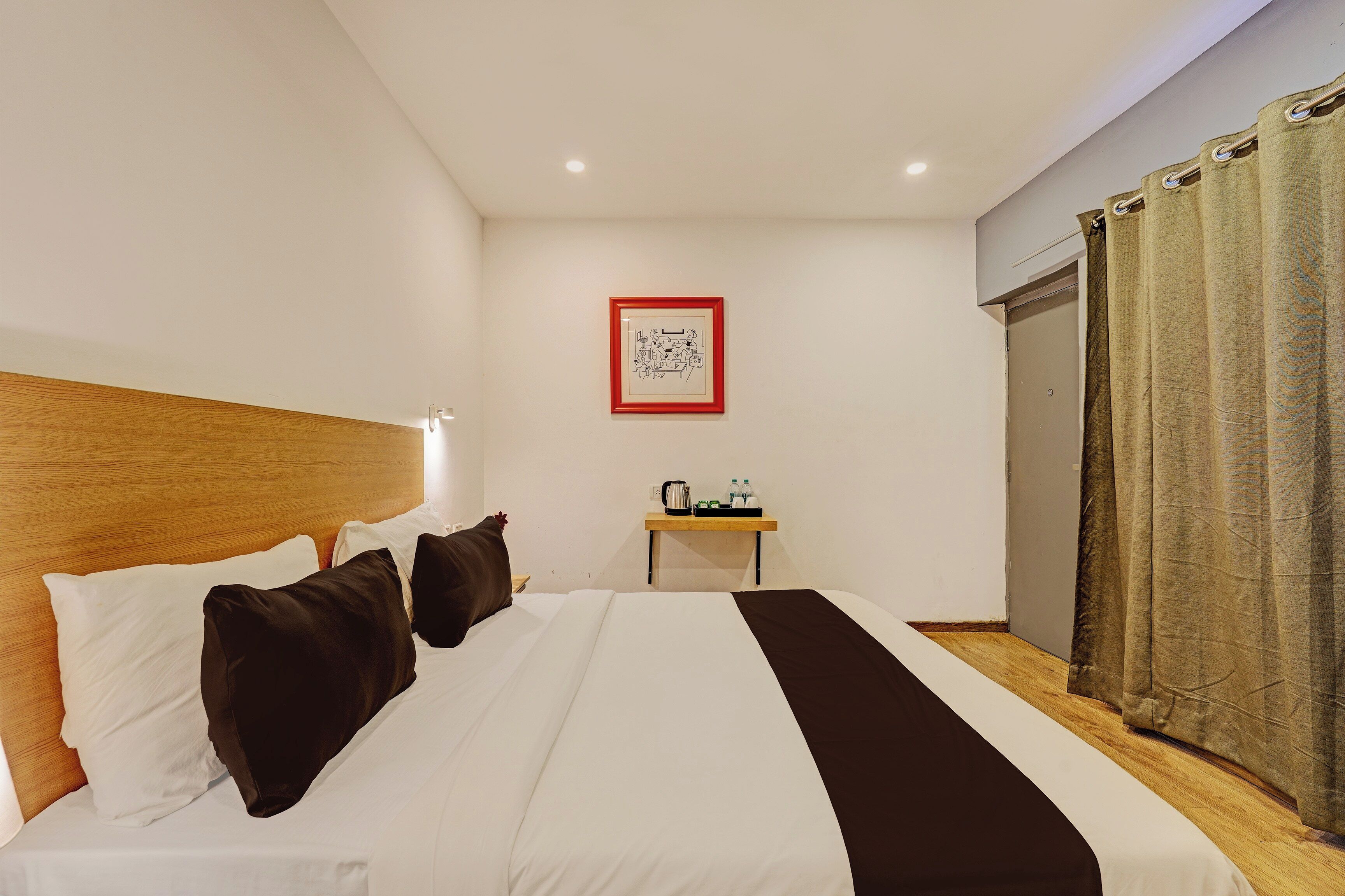 A hotel room with a bed, a bedside table, a framed picture on the wall, and a window with curtains.