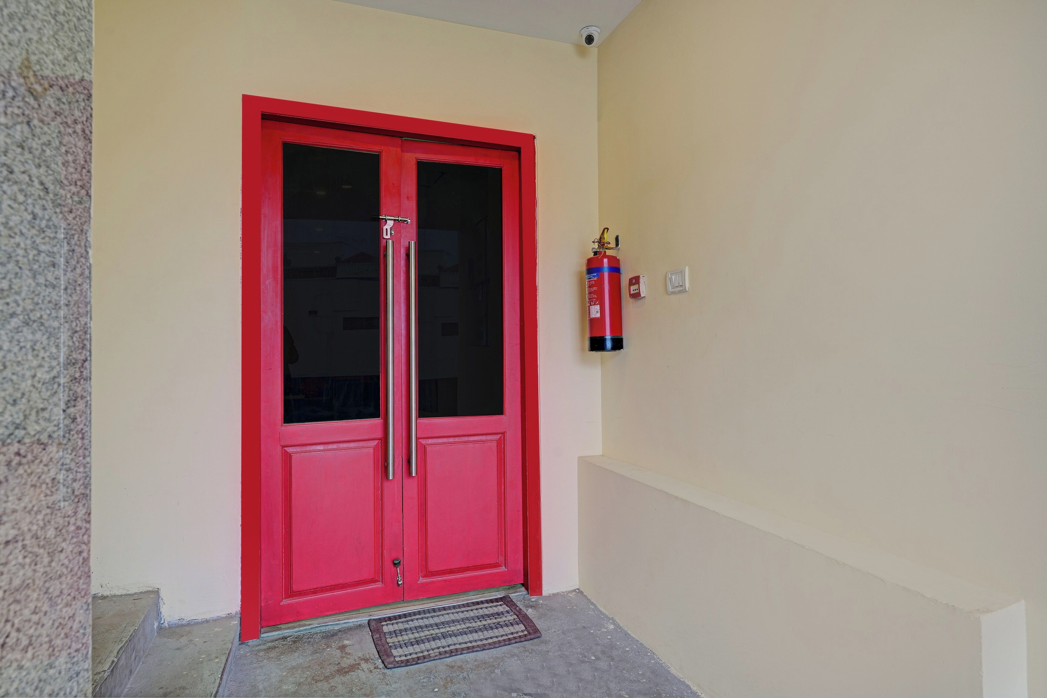 A red door with a fire extinguisher mounted on the wall beside it.