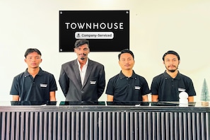 Four individuals standing behind a counter with a sign above them that reads 'TOWNHOUSE & Company-Serviced'. - Townhouse Ramamurthy Nagar (Bangalore)