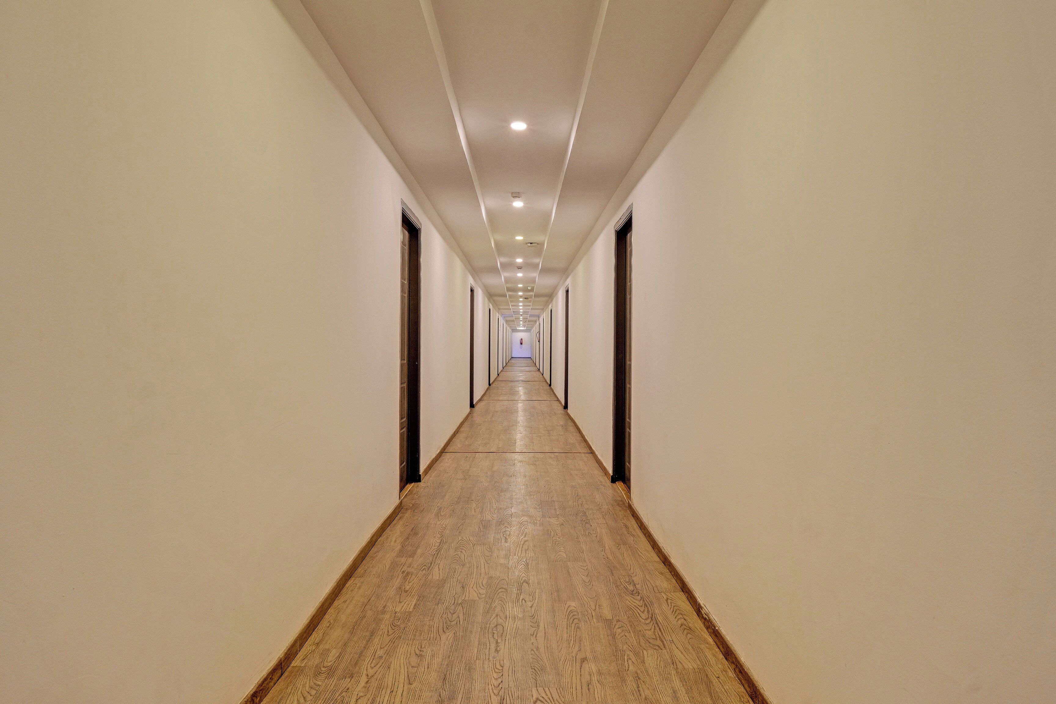 A long, narrow hotel corridor with wooden flooring and white walls.