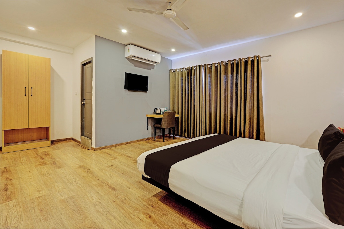 A hotel room with a bed, a desk, a chair, an air conditioning unit, and a television.