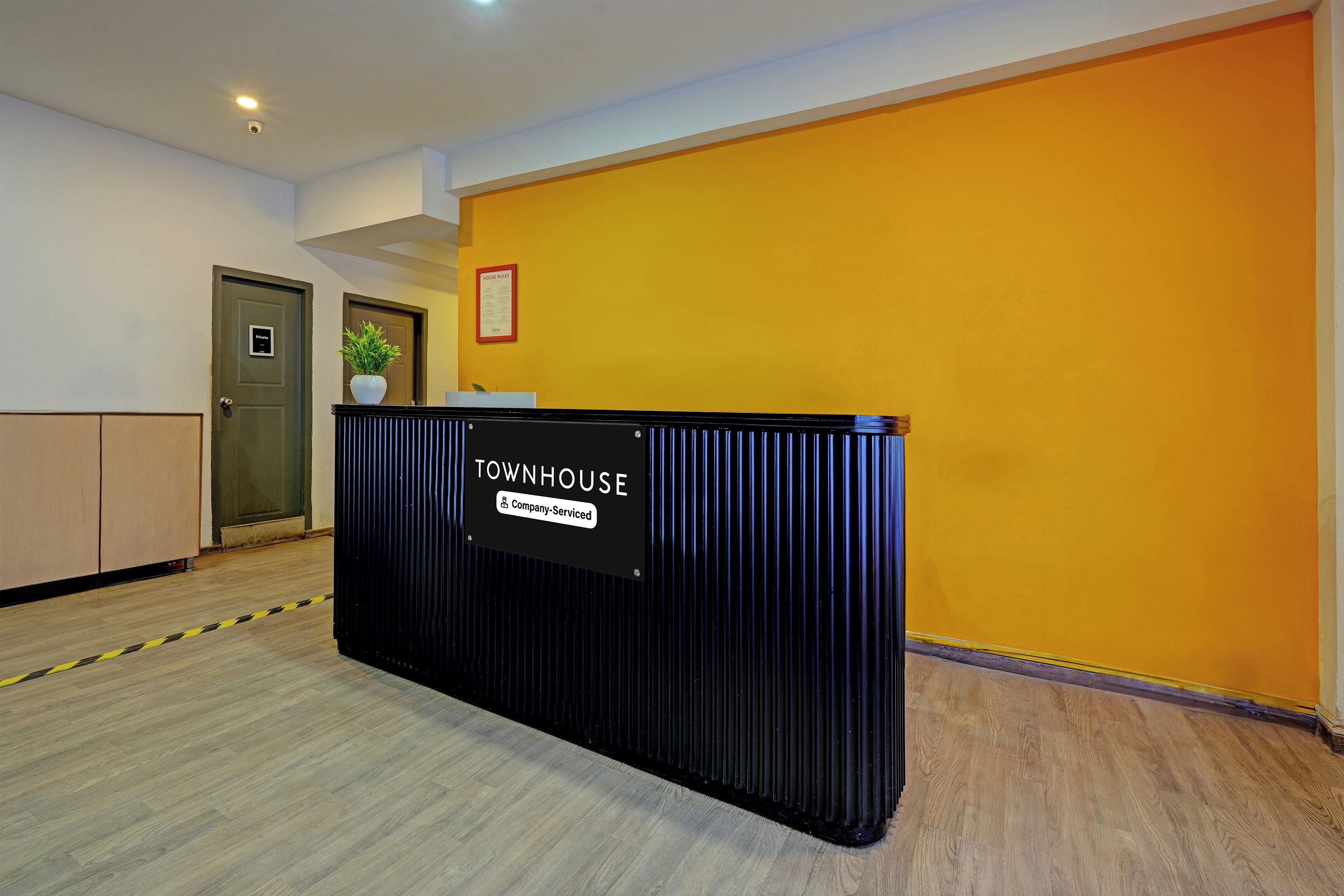 A reception desk labeled 'TOWNHOUSE' with a 'Company-Serviced' sign, a 'HOUSE RULES' notice, and a 'Private' door to the left.