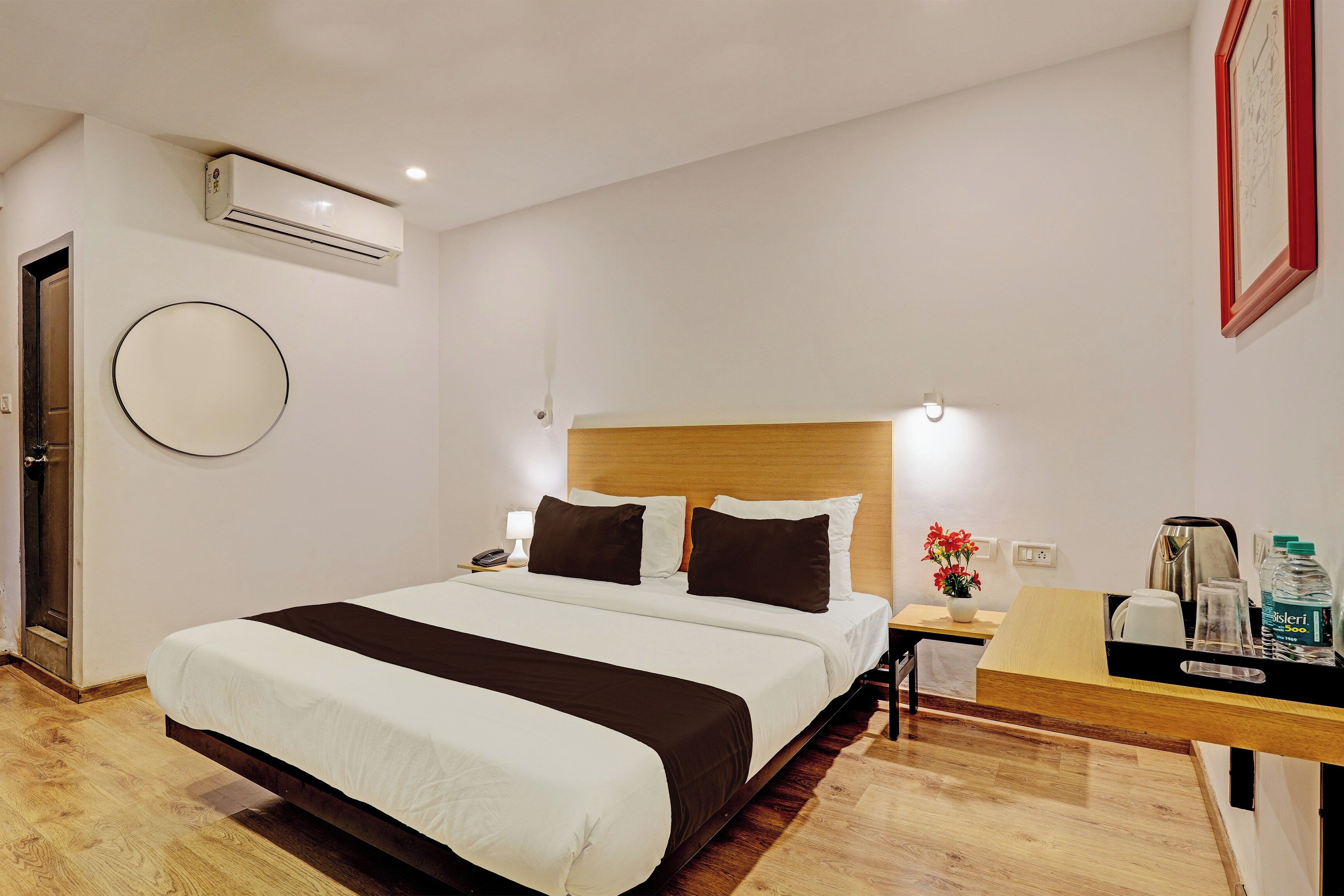 A hotel room with a bed, bedside table, lamp, and a wall-mounted air conditioner.