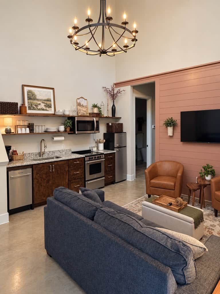 A modern kitchen with built-in appliances, a dining area with a sofa and chairs, and a television mounted on the wall.